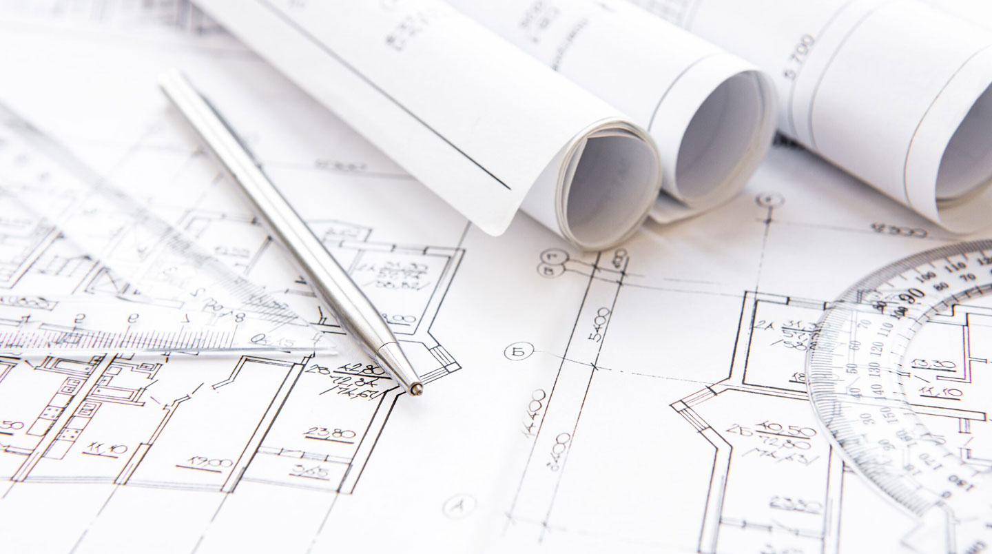 Plans architecturaux et documents de permis de construction de la Ville d'Outremont étalés sur une table de travail avec règle d'échelle et tablette numérique